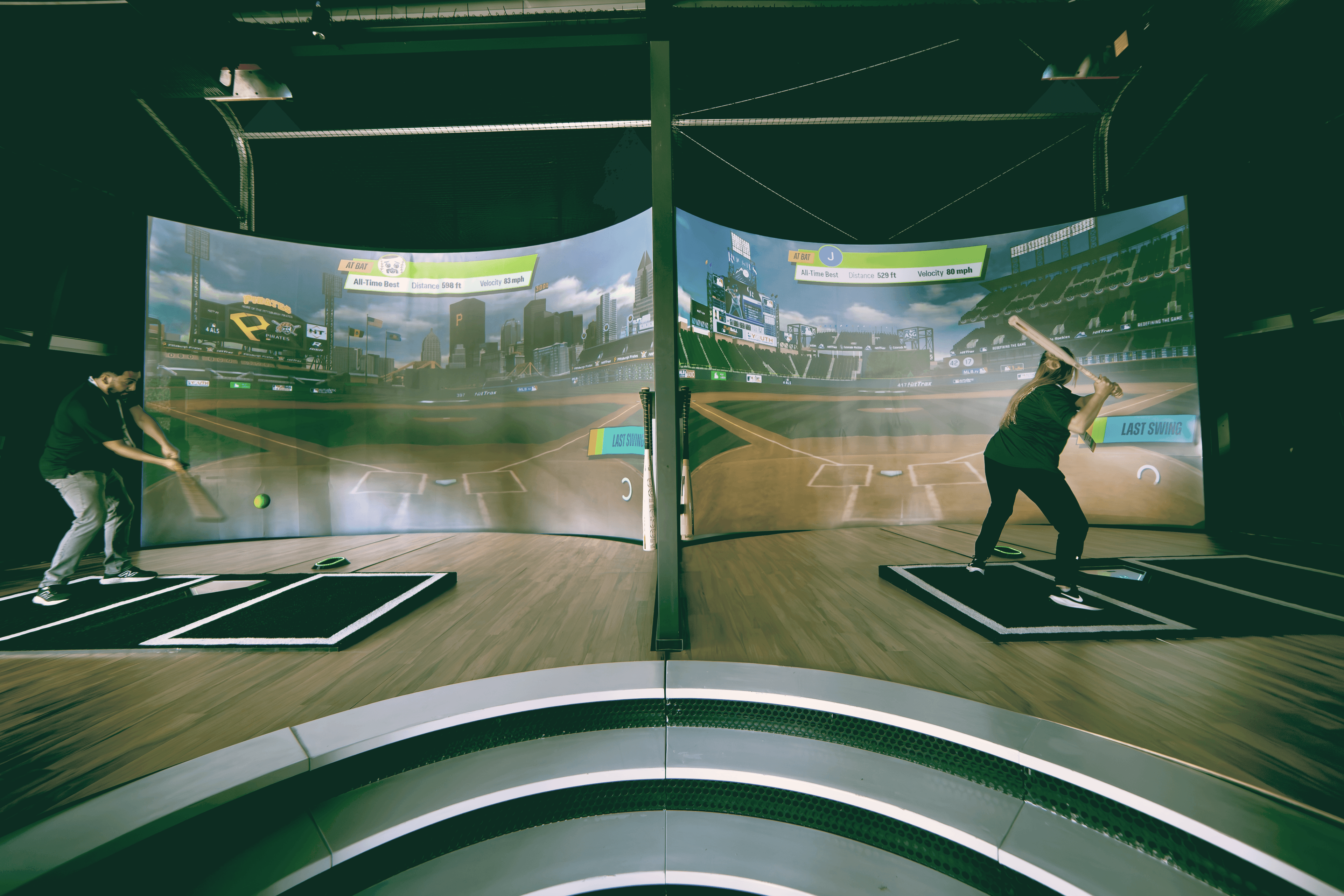 Two players batting side-by-side inside Home Run Dugout bays